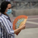 Imagen de archivo de una mujer con mascarilla que se abanica mientras camina durante un episodio de altas temperaturas en Sevilla