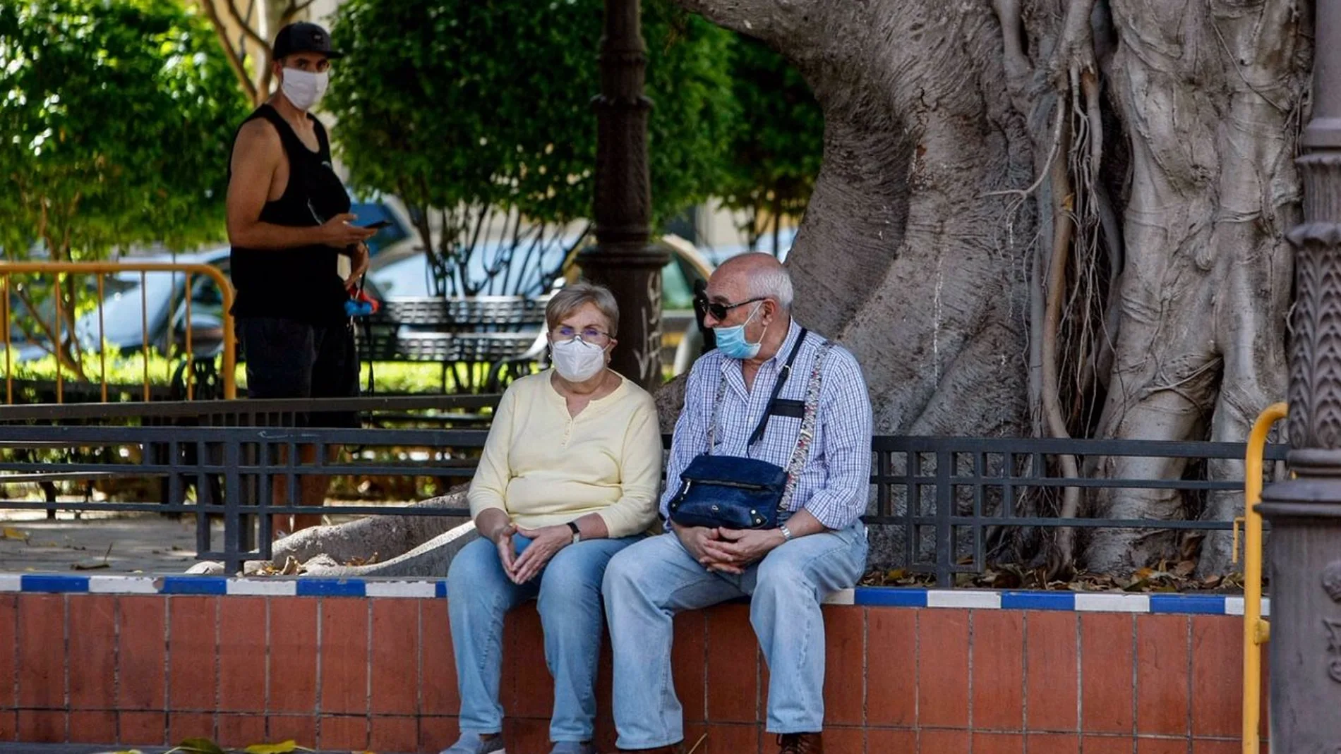 Dos personas mayores con mascarillas y sentadas en la calle en Sevilla