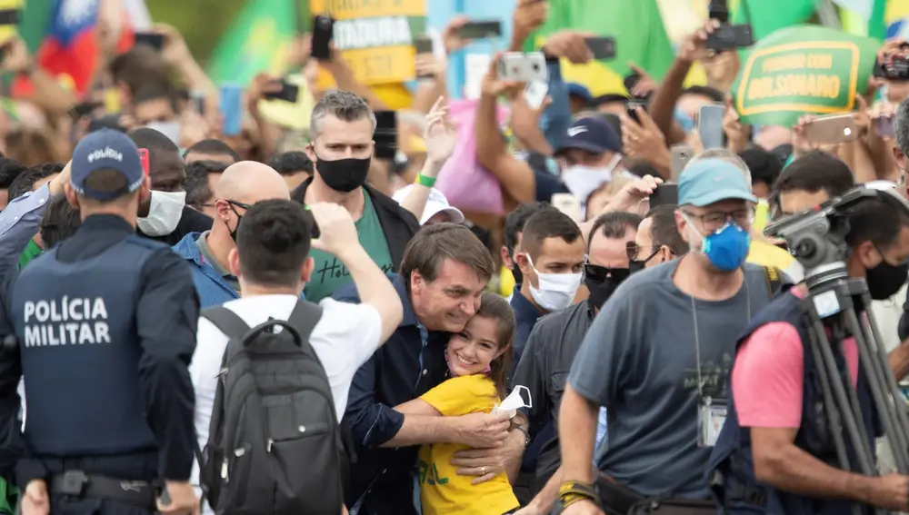 El presidente de Brasil, Jair Bolsonaro, saluda a una niña este domingo, en Brasilia. Cientos de seguidores del presidente se aglomeraron este domingo cerca del palacio de Gobierno para alabar a su ídolo, que sin protección se mezcló entre la multitud, ignorando de nuevo las recomendaciones por el COVID-19, una pandemia que no es prioridad para el mandatario
