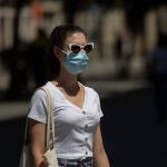 Una mujer con mascarilla y gafas de sol pasea por la calle.