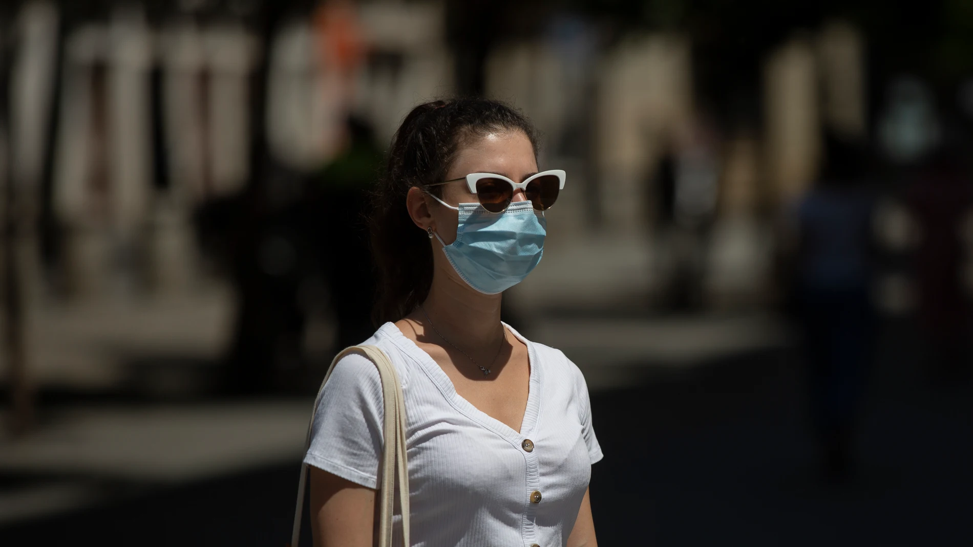 Una mujer con mascarilla y gafas de sol pasea por la calle.