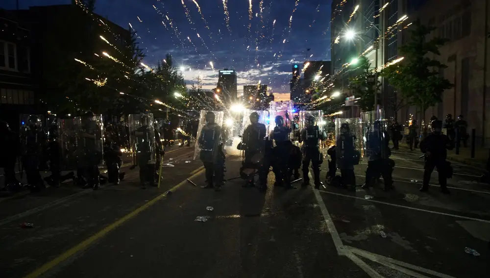 La Policía antidisturbios se protege de los fuegos artificiales lanzados por los manifestantes