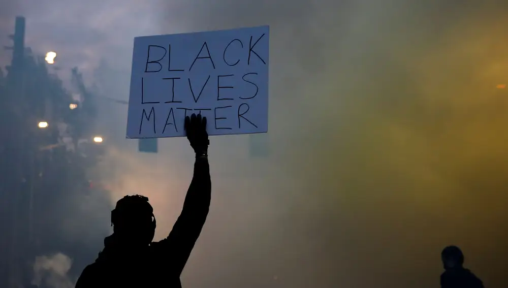 Un cartel de &quot;Black Lives Matter&quot; entre una cortina de gas lacrimógeno en Seattle, ayer