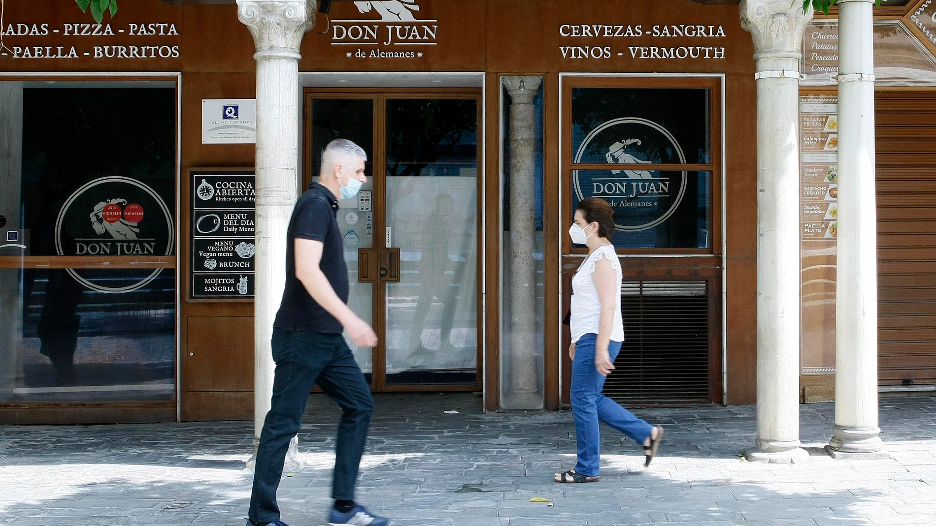 Dos personas, equipadas con mascarillas, se cruzan en una calle de Sevilla