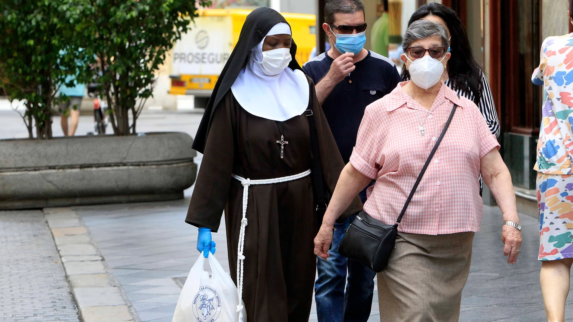 Varias personas, entre ellas una monja con mascarillas y guantes, recorren por el centro de Sevilla