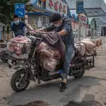 Hombres con máscaras protectoras cargan un scooter con carne al lado del edificio cerrado del mercado Xinfadi en el distrito de Fengtai, Beijing, China