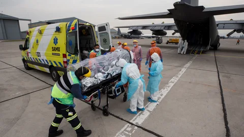Personal sanitario de la Fuerza Aérea de Chile (FACH) e integrantes del Servicio de Atención Médica de Urgencia SAMU (de naranja) llevan a un avión a un paciente crítico de COVID-19