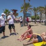 Dos auxiliares informan a unas personas sentadas en la arena de la playa de Marbella (Málaga) sobre las medidas de seguridad y la necesidad de guardar distancias.