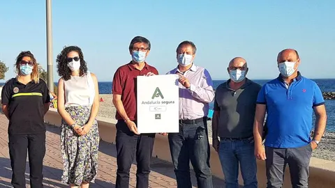 El delegado territorial de Turismo, José Luis Delgado y el alcalde del municipio, Manuel Cortes, junto a otros representantes del Consistorio y la responsable de Protección Civil, presentan el distintivo en una playa de Adra