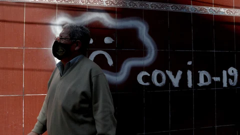 A man wearing a mask to curb the spread of the new coronavirus walks past COVID-19 graffiti, in La Paz, Bolivia, Wednesday, June 24, 2020. (AP Photo/Juan Karita)