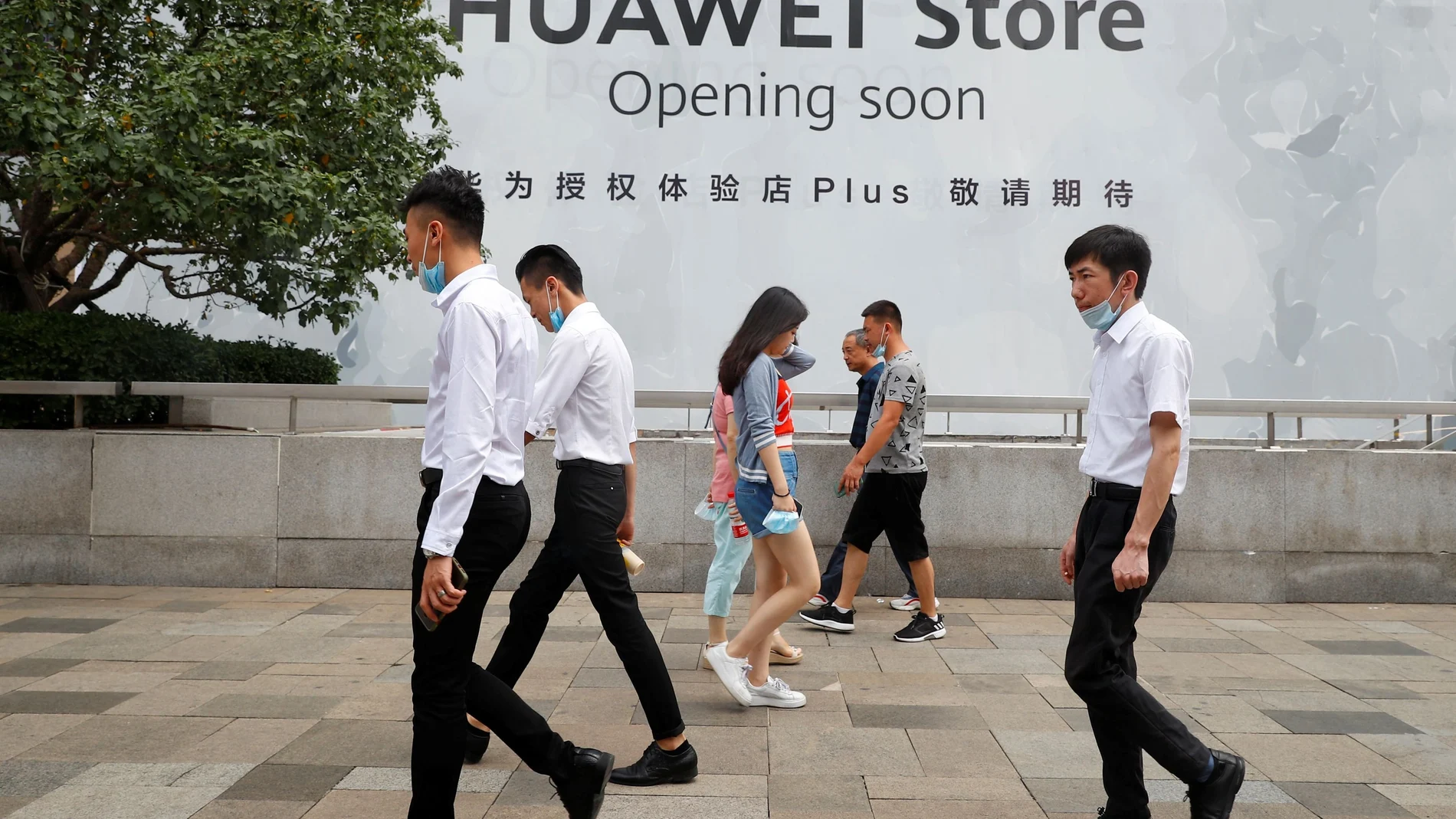 People walk past an advertisement announcing the opening of a HUAWEI store in Beijing