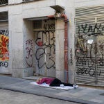 Una persona sin techo tendida en el suelo intenta dormir ante un establecimiento que ha cerrado por la pandemia