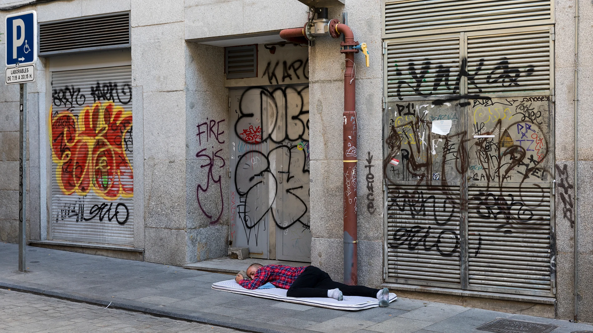 Una persona sin techo tendida en el suelo intenta dormir ante un establecimiento que ha cerrado por la pandemia