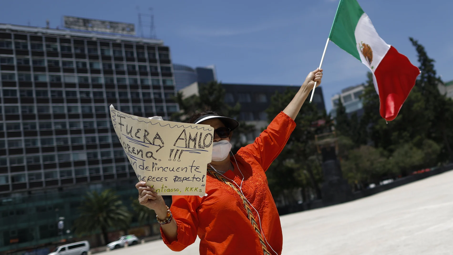 A demonstrator holds up a sign calling for the resignation of President Andres Manuel Lopez Obrador, as she stands along the road during a anti-government driving protest by hundreds of cars, in Mexico City, Sunday, June 28, 2020. (AP Photo/Rebecca Blackwell)