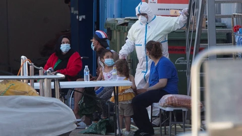 Un sanitario equipado con equipo de protección integral da instrucciones a varios inmigrantes esta tarde en el Centro Integrado de Inmigrantes del Puerto de Santa Lucía, en Cartagena.