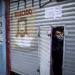 Romeo Mendoza peers from behind the door of his clothing shop, open only to phone and online orders, during a government-ordered lockdown to curb the spread of the new coronavirus in Buenos Aires, Argentina, Friday, June 26, 2020. Buenos Aires and its surrounding area will start on Wednesday, July 1st, a stricter quarantine as the country braces for a further economic slowdown due to the lockdown. (AP Photo/Natacha Pisarenko)