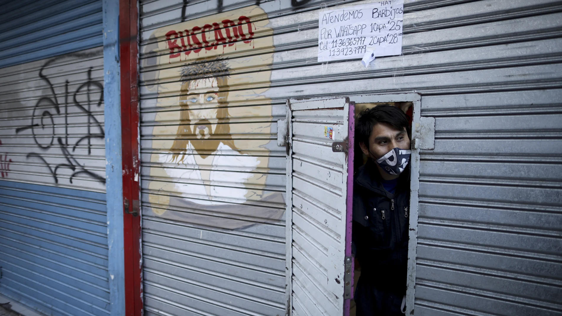 Romeo Mendoza peers from behind the door of his clothing shop, open only to phone and online orders, during a government-ordered lockdown to curb the spread of the new coronavirus in Buenos Aires, Argentina, Friday, June 26, 2020. Buenos Aires and its surrounding area will start on Wednesday, July 1st, a stricter quarantine as the country braces for a further economic slowdown due to the lockdown. (AP Photo/Natacha Pisarenko)