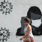 Una mujer camina sobre un mural de Jair Bolsonaro con mascarilla y una imagen del virus con su rostro