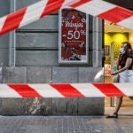 Una persona protegida con mascarilla pasa al lado del escaparate de una tienda donde se observan carteles indicativos de rebajas en Valencia