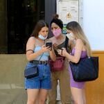 Tres jóvenes con mascarillas conversan con sus móviles en mano