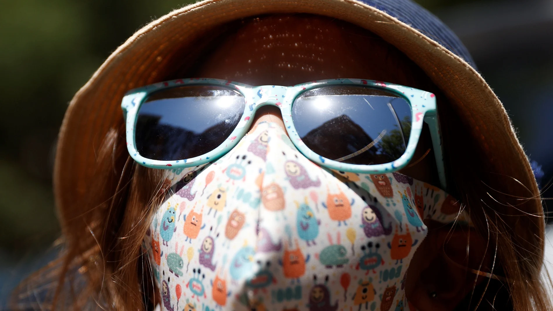 Una niña con mascarilla y con sombrero para protegerse del calor