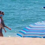 Dos jóvenes pasean con la mascarilla puesta por la orilla de la playa