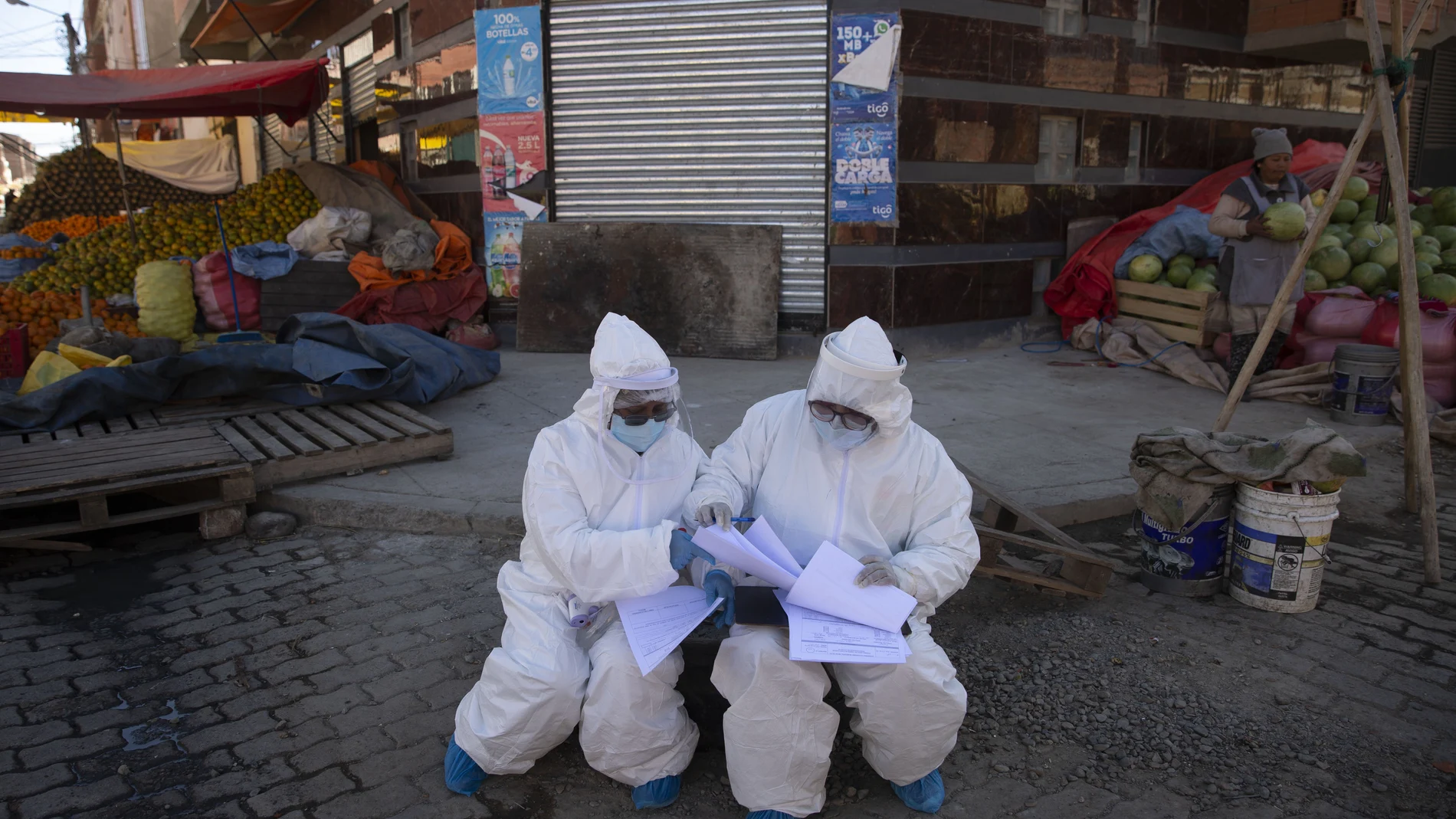 Healthcare workers dressed in full protective gear organize their documents of data they have collected during a house-to-house new coronavirus testing drive, ringed by a produce market in the Villa Dolores neighborhood of El Alto, Bolivia, Saturday, July 18, 2020. (AP Photo/Juan Karita)