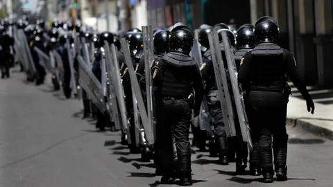 Police in riot gear assemble at a distance, as a handful of protesters stopped traffic in Paseo de la Reforma, one of central Mexico City's main thoroughfares, Saturday, July 18, 2020. The few protesters carried signs condemning the president's Maya Train project, and calling for the release of people detained during previous violent anarchist protests. (AP Photo/Marco Ugarte)