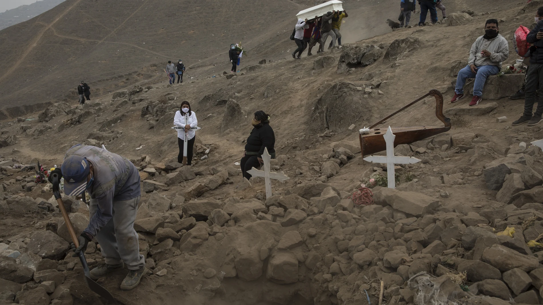 FILE - In this May 27, 2020, file photo, a cemetery worker shovels dirt into a grave that contains the remains of Apolonia Uanampa, who died from the coronavirus, as the coffin that contains the remains of Demetria Huamani, also a victim of the virus, is carried to her burial site at the Nueva Esperanza cemetery on the outskirts of Lima, Peru. A new snapshot of the frantic global response to the coronavirus pandemic shows some of the world's largest government donors of humanitarian assistance are buckling under the strain and overall aid commitments have dropped by a third from the same period last year. (AP Photo/Rodrigo Abd, File)