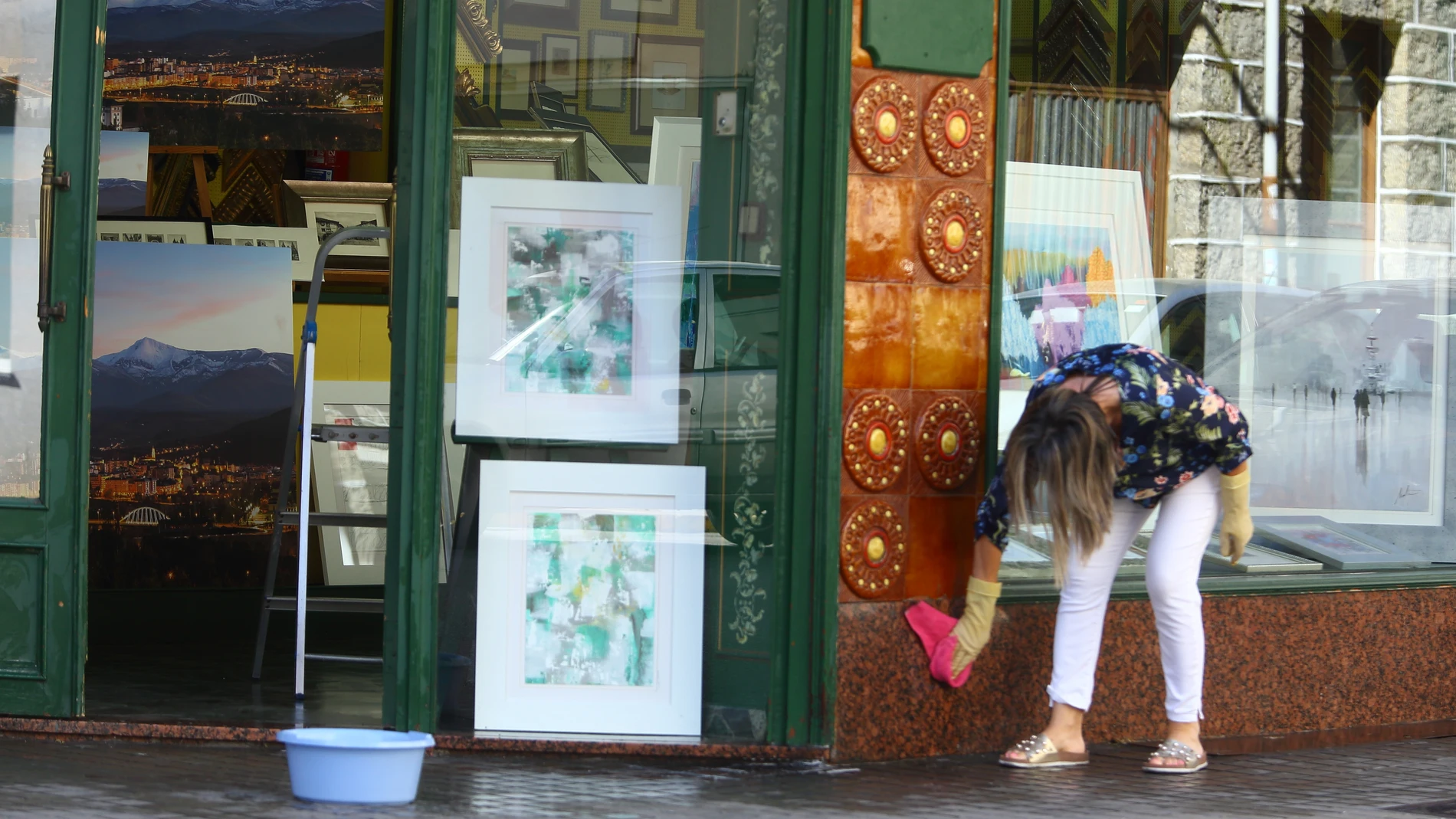 Una mujer limpia la fachada de su comercio en Ponferrada