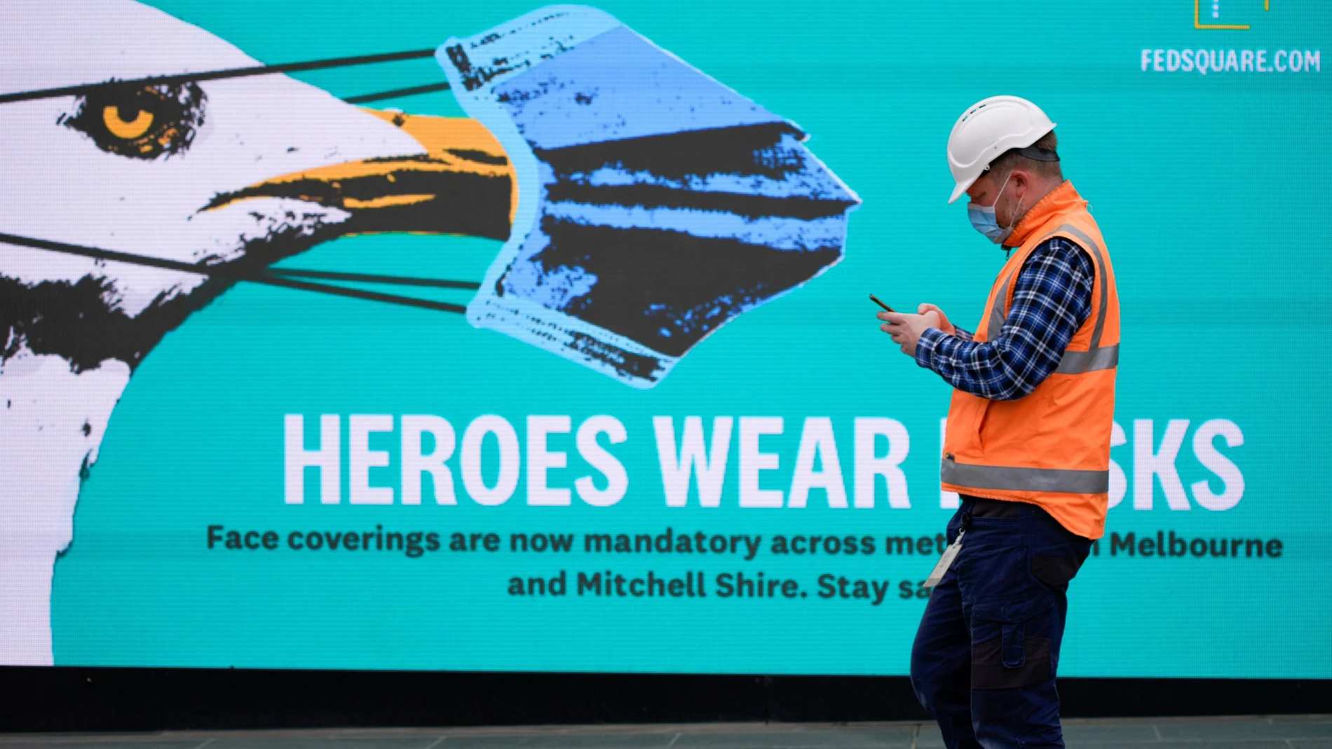 FILE PHOTO: An essential worker wearing a face mask walks past a 'Heroes Wear Masks' sign in Melbourne, the first city in Australia to enforce mask-wearing to curb a resurgence of COVID-19