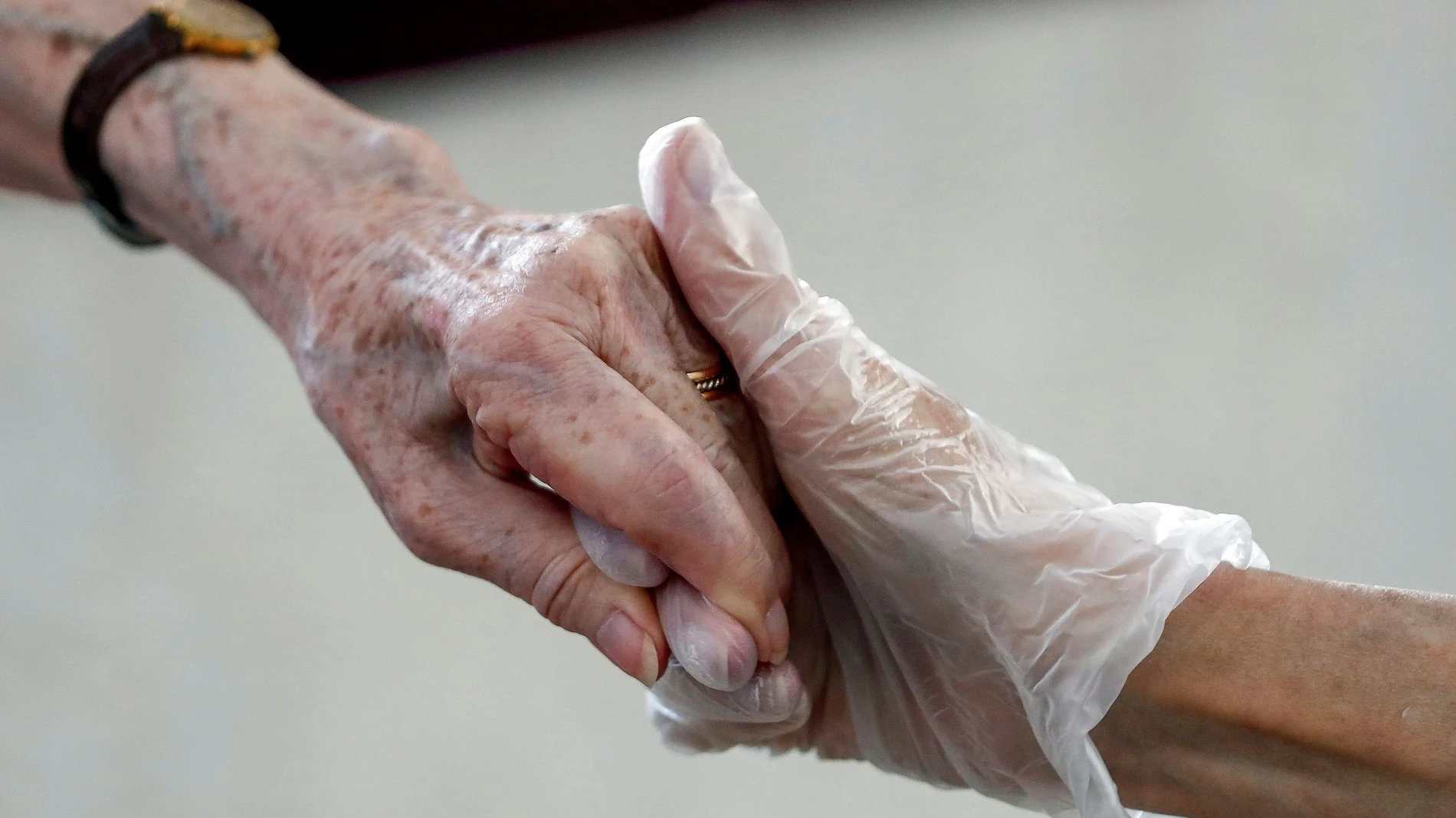 Una hija y una madre que permanece en una residencia de ancianos se dan la mano