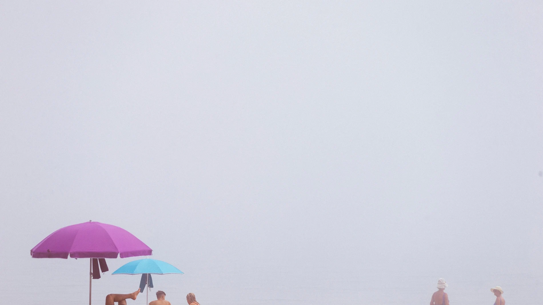 Varias personas disfrutan en la playa de la Malagueta (Málaga) a pesar del banco de taró, la niebla que entra desde el mar