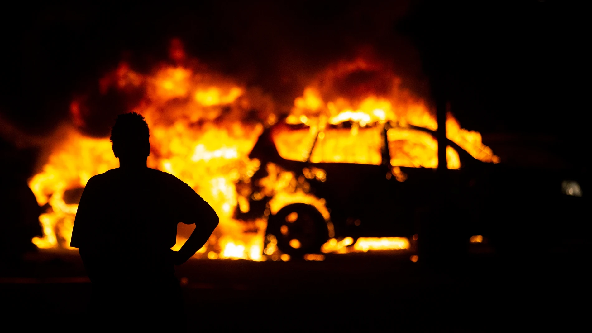 Un manifestante contempla la quema de vehículos durante las protestas en Kenosha