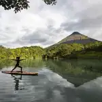 Una mujer practica yoga en una tabla en una laguna desde donde se aprecia el volcán Arenal en la zona de la Fortuna de San Carlos el 28 de agosto de 2020, al norte de San José (Costa Rica)