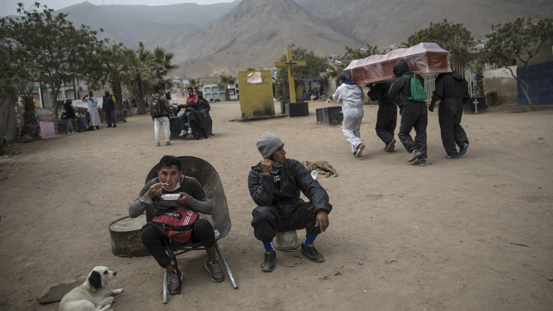 A cemetery worker sits in his wheelbarrow during his lunch breaj as fellow workers walk past shouldering a casket that contains the remains of a person who is suspected to have died from symptoms related to the new coronavirus, at the "Martires 19 de Julio" cemetery, in Comas, on the outskirts of Lima, Peru, Saturday, July 4, 2020. Along with cremations, burials have continued, with nearly 200 deaths daily due to a rate of infection that continues to be among the worldâ€™s highest. Many families must hunt down spots in economical and far-flung cemeteries on the outskirts of Lima. (AP Photo/Rodrigo Abd)