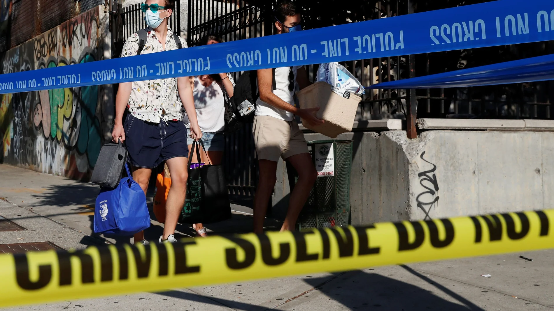 People walk with protective face masks behind NYPD police tape, where according to local media reports five people were shot, including a 6-year-old boy, early Monday during an outdoor J?Ouvert celebration, in the Crown Heights section Brooklyn in New Yo
