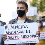 El cofundador de Podemos y director del Instituto 25 de Mayo del partido morado, Juan Carlos Monedero, sostiene una pancarta donde se puede leer "Almeida amenaza el Rastro Histórico".