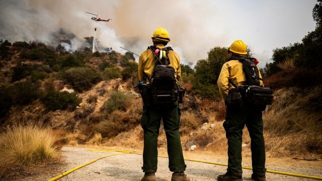Dos bomberos observan a un helicóptero que deja caer agua sobre el fuego Bobcat, ardiendo en el Bosque Nacional de Ángeles hoy, cerca de Arcadia, California (EE.UU.)