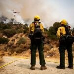 Dos bomberos observan a un helicóptero que deja caer agua sobre el fuego Bobcat, ardiendo en el Bosque Nacional de Ángeles hoy, cerca de Arcadia, California (EE.UU.)