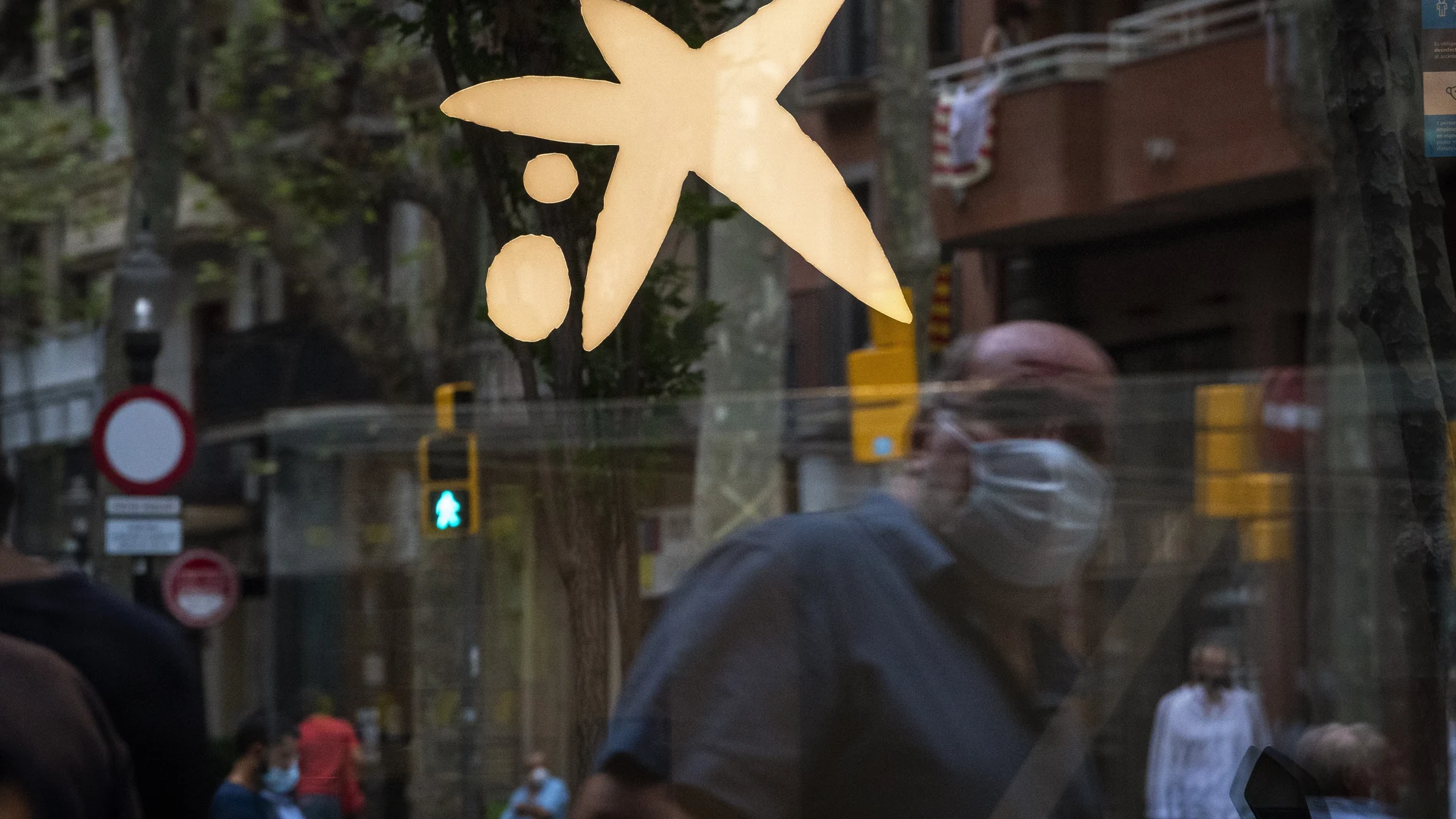 Un hombre con mascarilla pasa frente a una oficina de CaixaBank en Barcelona