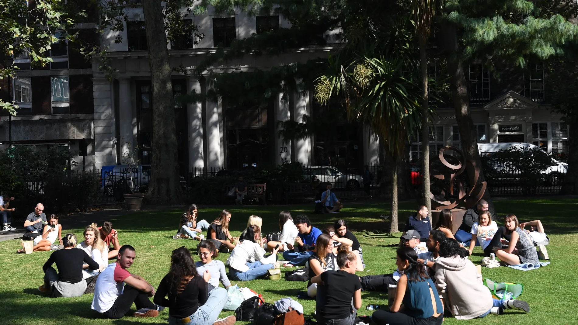 Gente sentada en la plaza del Soho en Londres sin respetar las distancias sociales