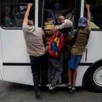 Varias personas se sujetan de la parte trasera de un autobús lleno de pasajeros debido a la suspensión del servicio del subterráneo por un corte de energía hoy, en Caracas
