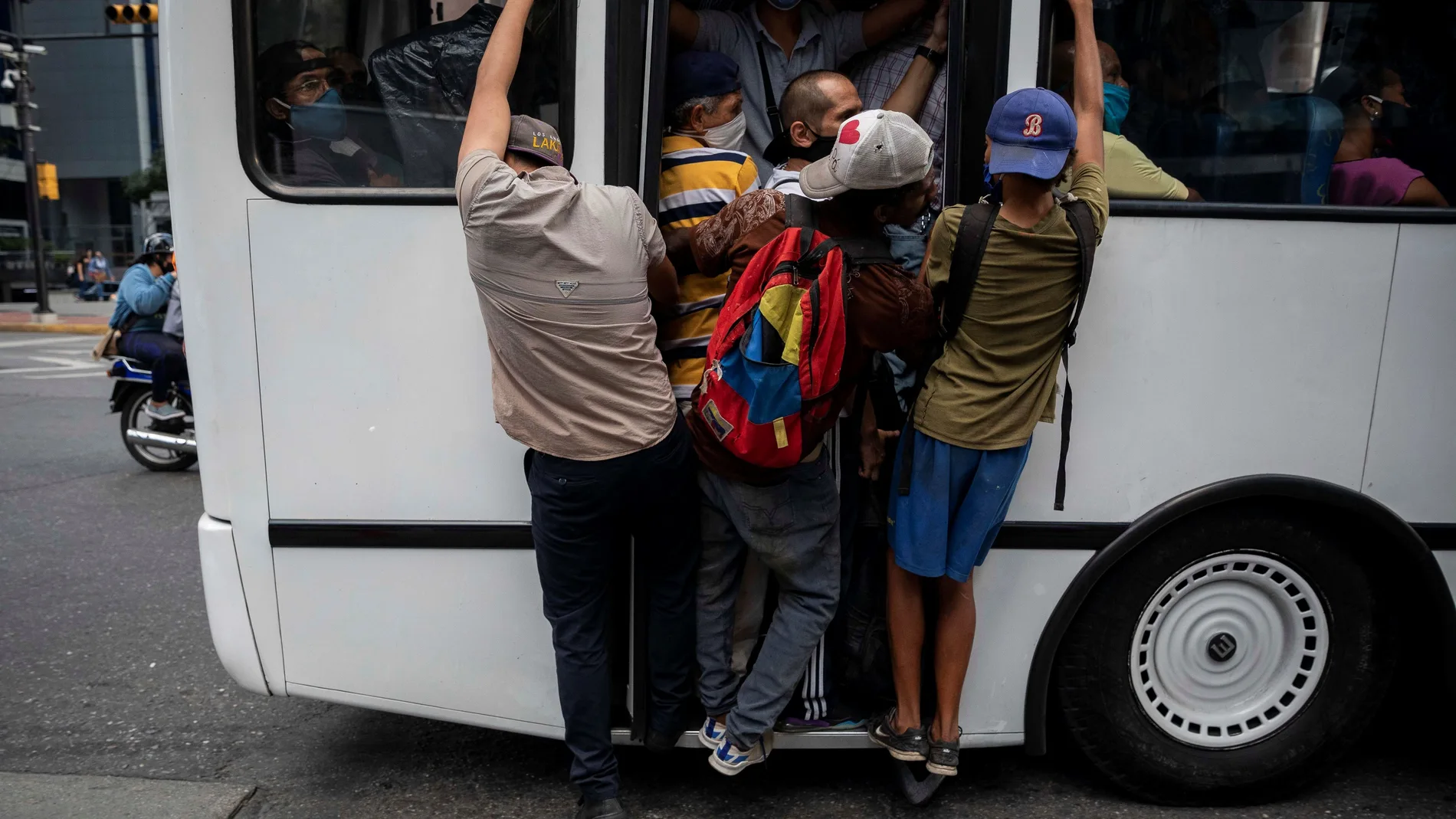 Varias personas se sujetan de la parte trasera de un autobús lleno de pasajeros debido a la suspensión del servicio del subterráneo por un corte de energía hoy, en Caracas