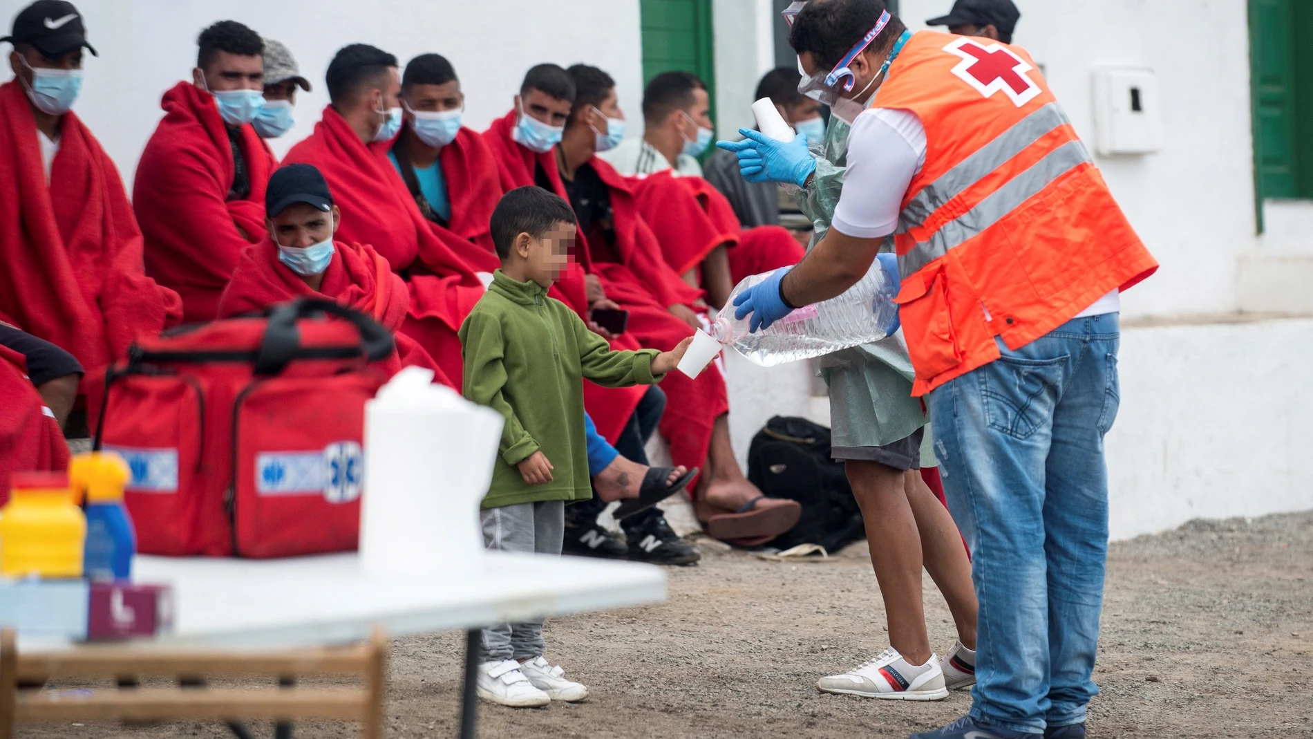 Miembros de los equipos de emergencias ofrecen agua y algo de comida a los 29 inmigrantes que han llegado en patera este viernes a la costa de Caleta de Caballo, en el norte de Lanzarote, entre ellos una mujer y seis menores
