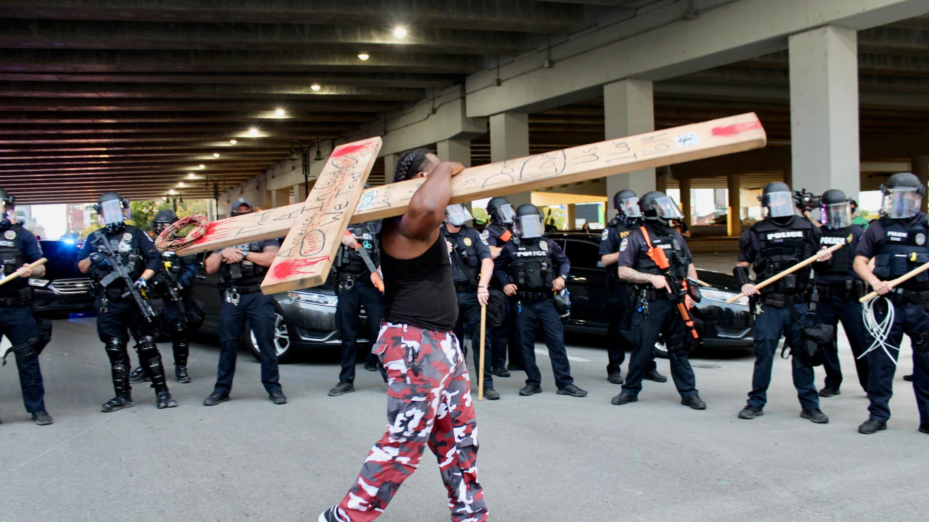 Un hombre carga con una cruz frente al cordón policial en Louisville