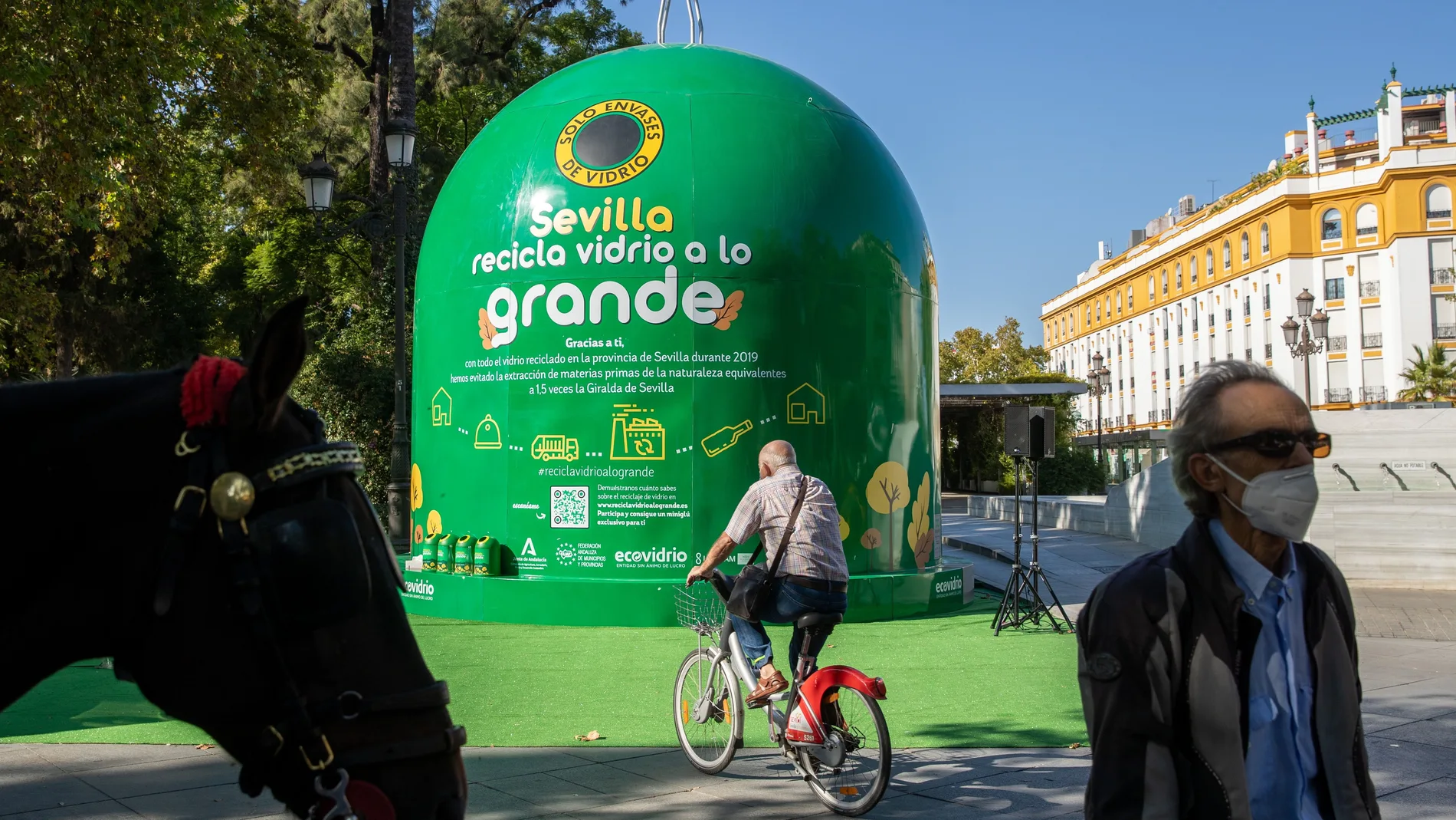 Varias personas pasan junto al contenedor de reciclaje de vidrio más grande del mundo instalado en los Jardines de Cristina en Sevilla