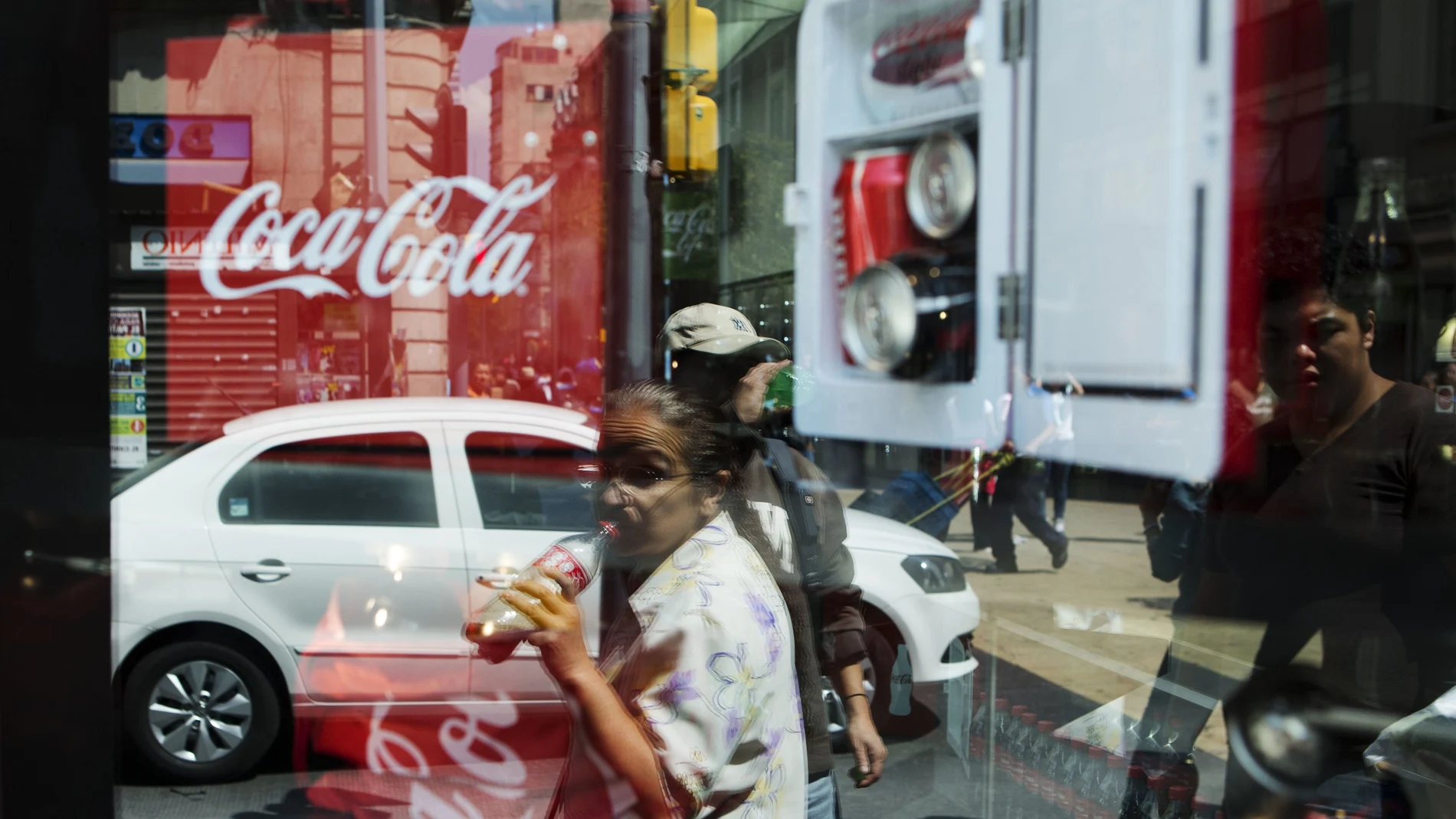 Una mujer bebe una bebida azucarada mientras camina por Ciudad de México bajo un cártel de Coca-cola