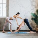 En la imagen, dos chicas practican posturas de yoga para tonificar.