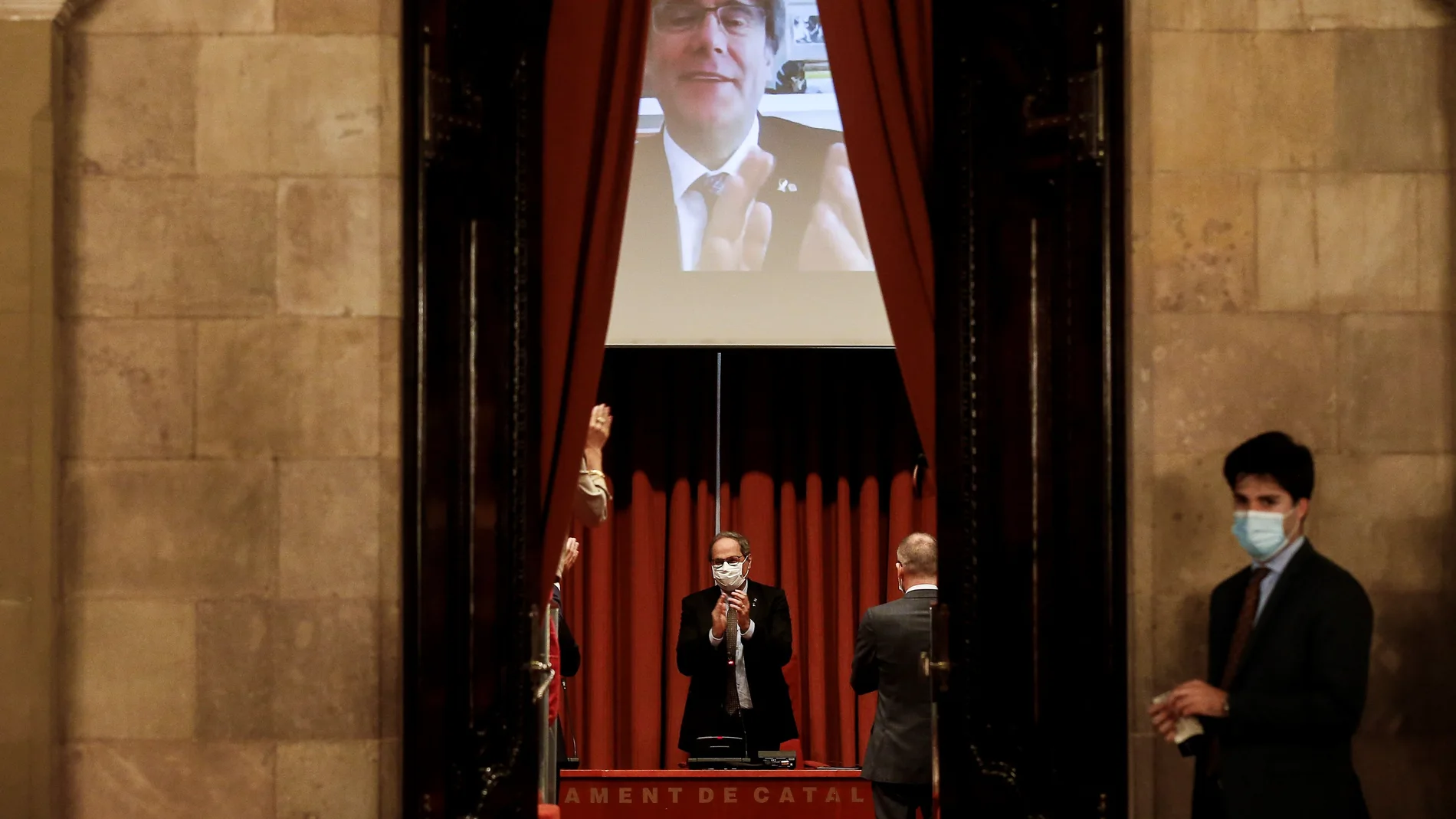 GRAFCAT2307. BARCELONA, 30/09/2020.- El expresidente de la Generalitat, Quim Torra, recibe el aplauso del expresidente Carles Puigdemont (en la pantalla) y los diputados de JxCat a su llegada a la reunión que han mantenido en el Parlament, previa al pleno específico para abordar su inhabilitación, en el que comparece en la cámara catalana como invitado y podrá intervenir durante la sesión. EFE/Quique Garcia
